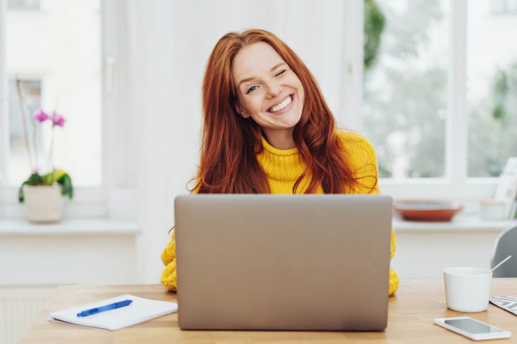 Junge fröhliche rothaarige Frau mit Laptop im hellen Zimmer tages-geld.net Desktop_View